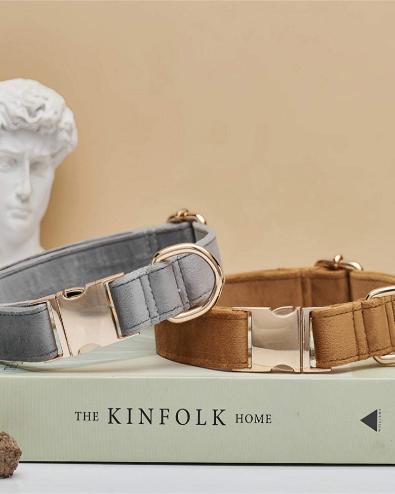 Two dog collars, one gray and one brown, on a book titled 'The Kinfolk Home' with a classical statue in the background.