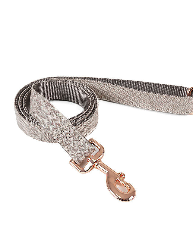Grey herringbone dog leash with rose gold clasp, coiled on a white background.