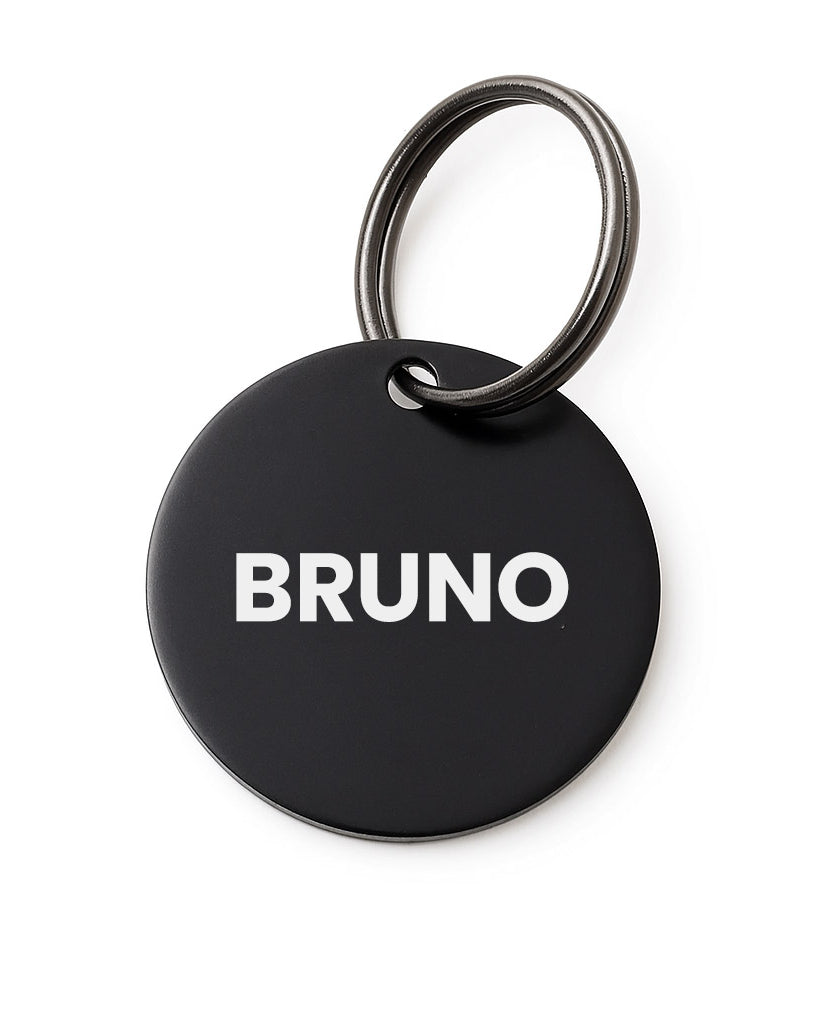 Black round pet tag with 'BRUNO' printed on it, featuring a silver ring.