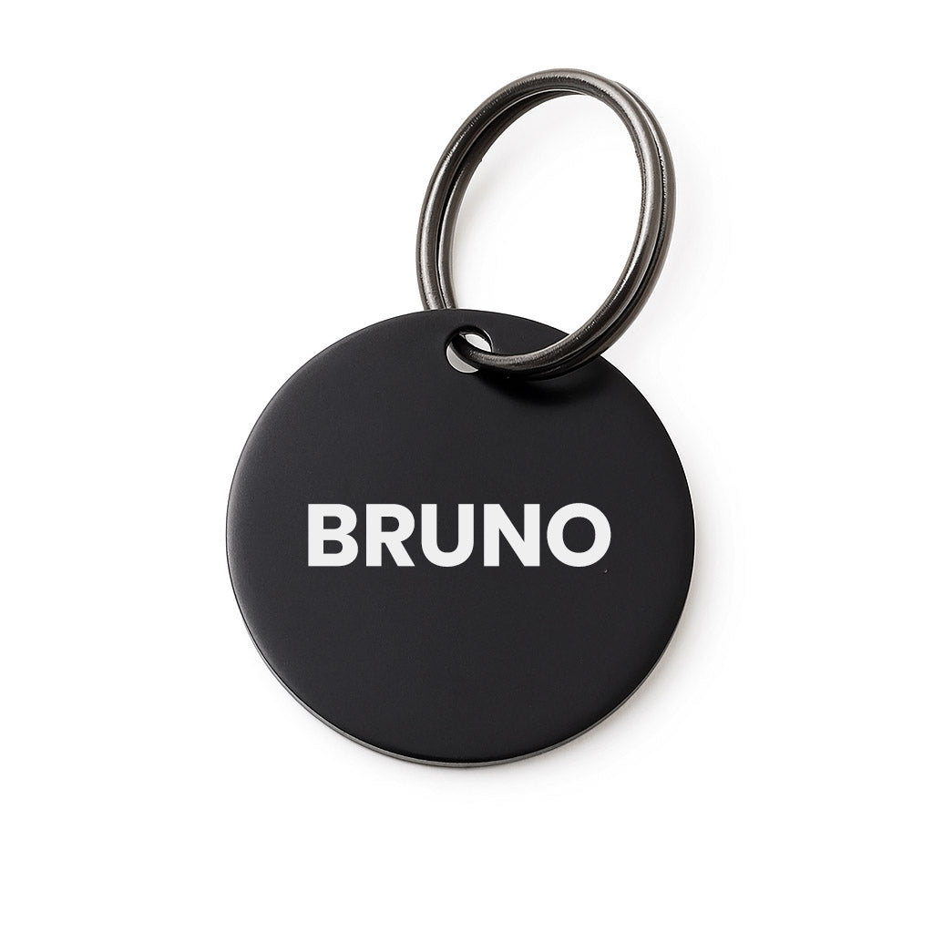Black round pet tag with 'BRUNO' printed on it, featuring a silver ring.