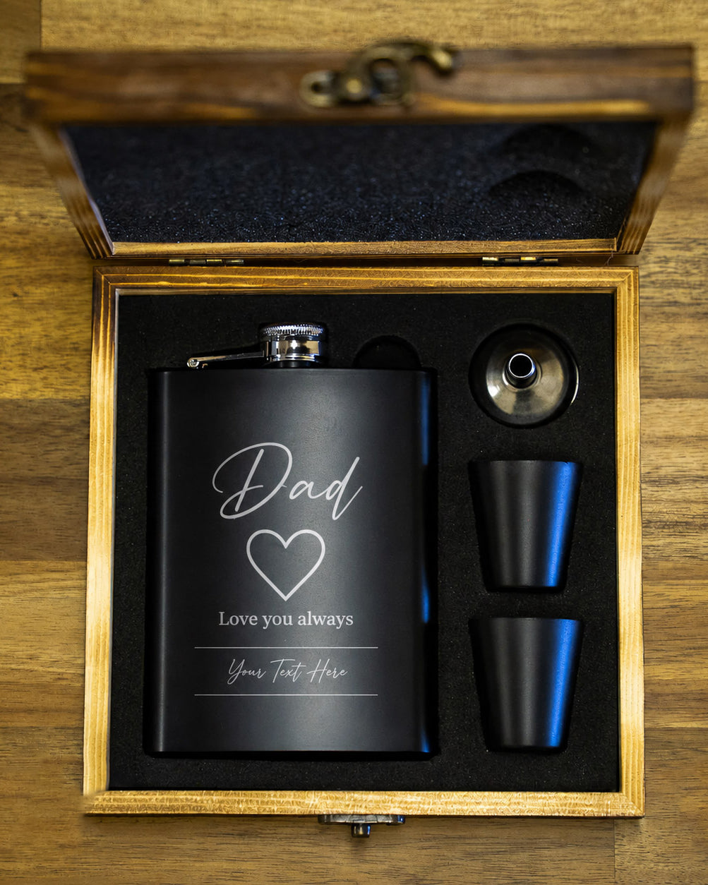 Black flask with engraved message in a wooden gift box on a wooden surface