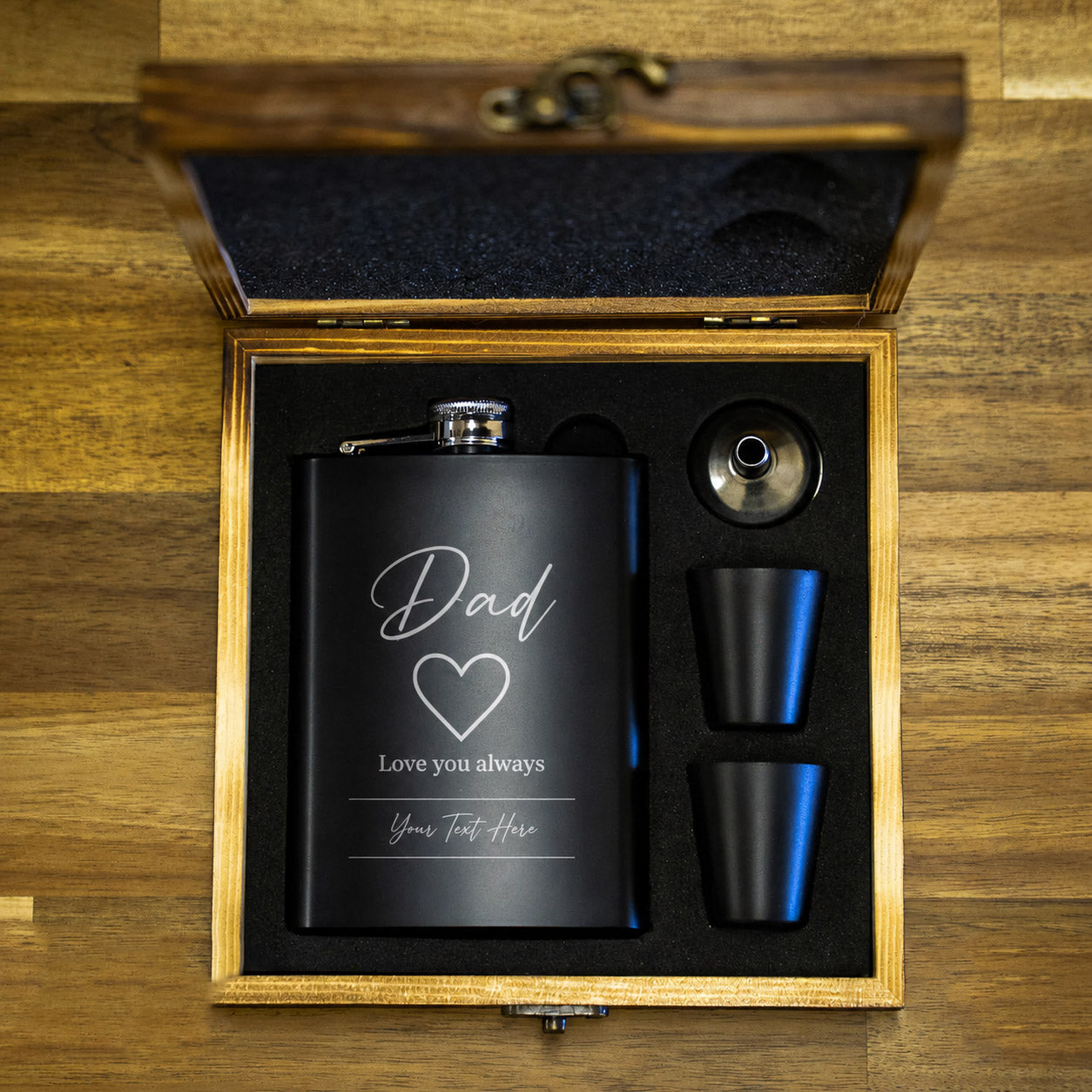 Black flask with engraved message in a wooden gift box on a wooden surface