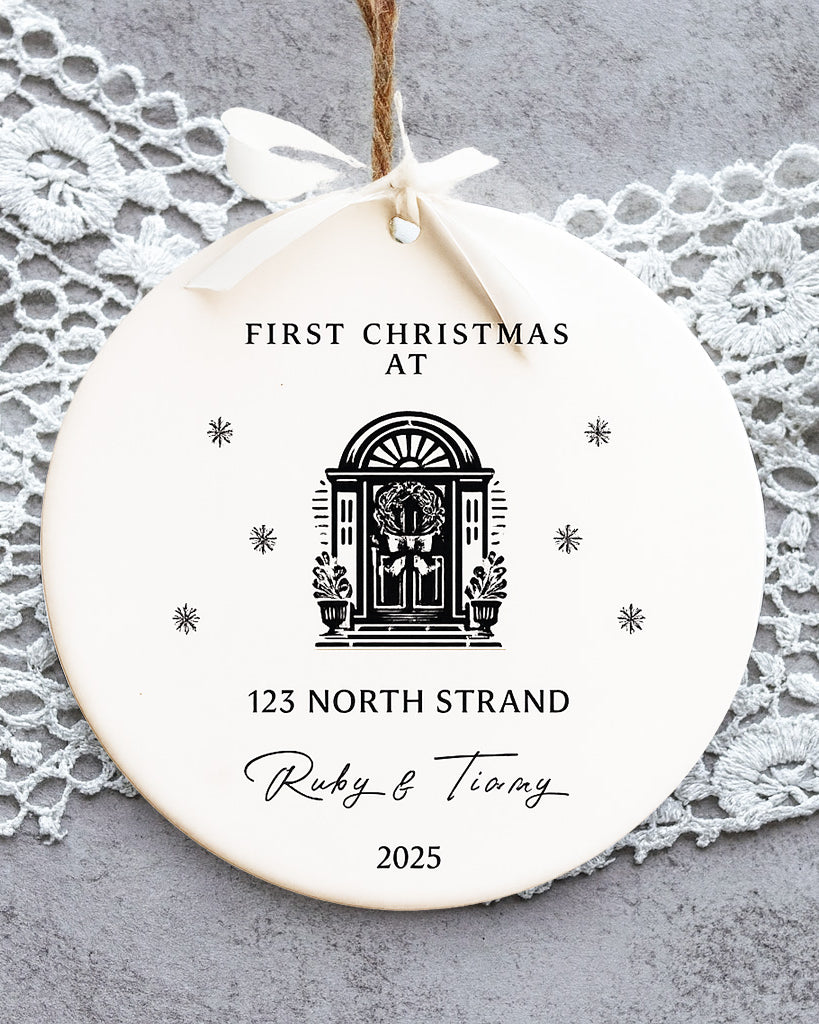 Round ceramic ornament with 'First Christmas at' text and design, hanging on a lace doily.