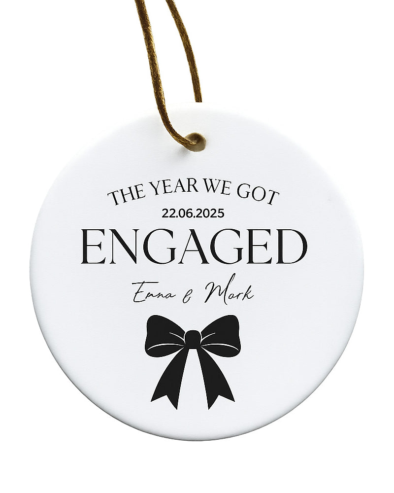 Round white ornament with black text and a bow design, featuring 'The Year We Got Engaged' and personalized names.