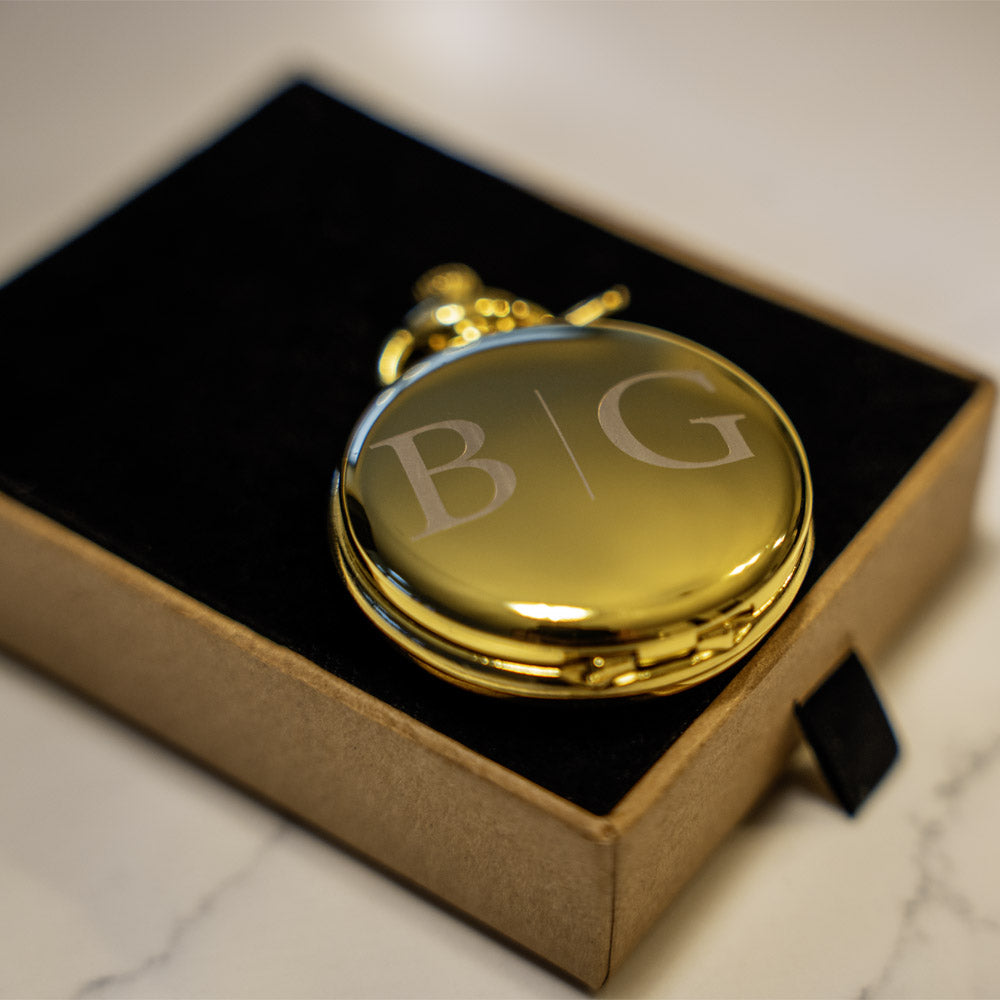 Gold pocket watch with 'B&G' initials in a box on a marble surface