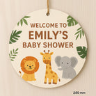 Round wooden sign with lion, giraffe, and elephant illustrations and text 'Welcome to Emily's Baby Shower' on a beige background.