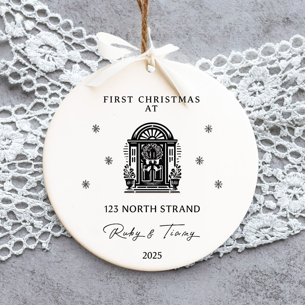 Round ceramic ornament with 'First Christmas at' text and design, hanging on a lace doily.