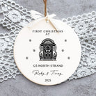 Round ceramic ornament with 'First Christmas at' text and design, hanging on a lace doily.