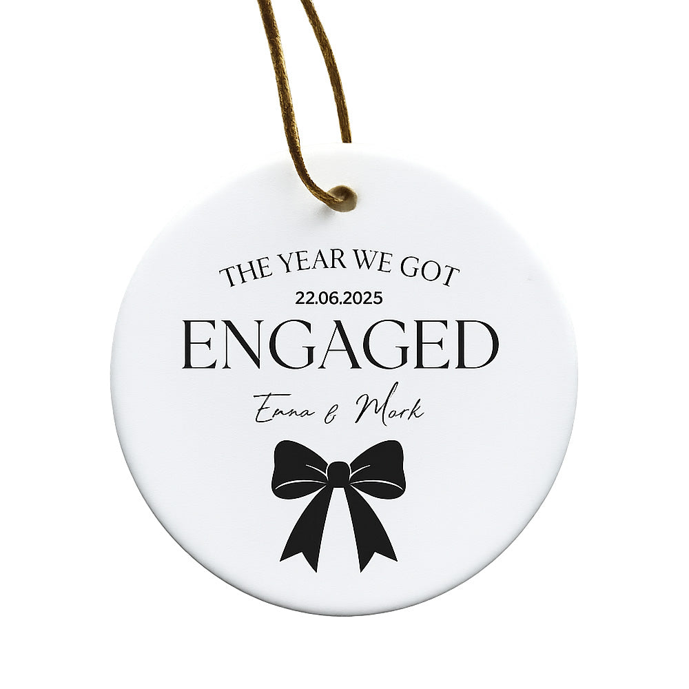 Round white ornament with black text and a bow design, featuring 'The Year We Got Engaged' and personalized names.